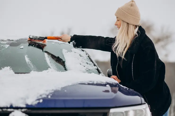 mujer-limpiando-nieve-coche Mujer con una escobilla limpiando la nieve y el hielo de su coche