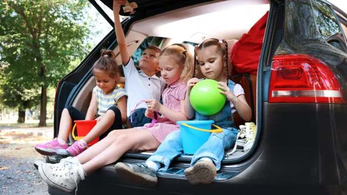 Cuatro niños de una familia sentados en el maletero de su coche familiar de ocasión